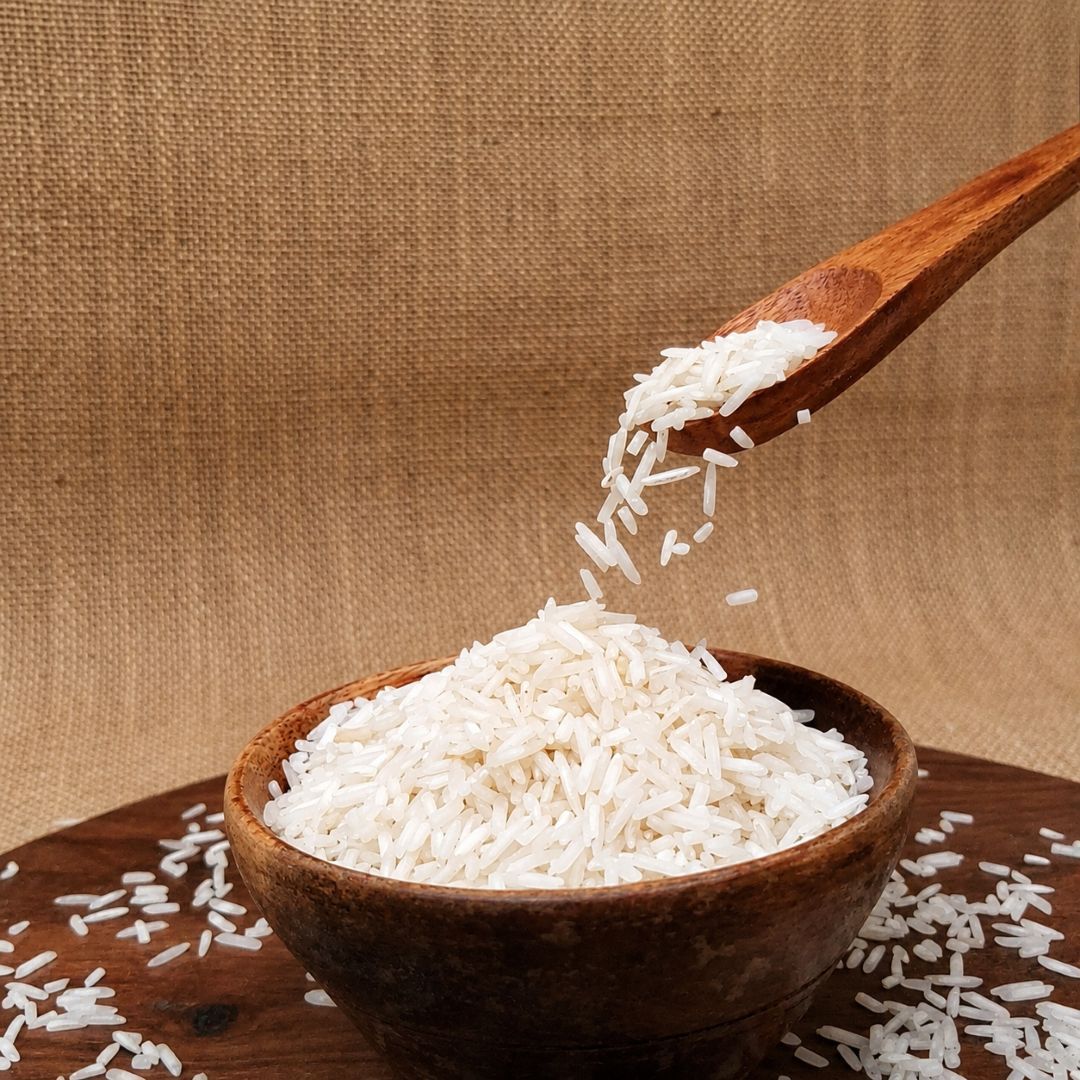 Basmati Standard rice grains pouring from a wooden spoon into a bowl, showcasing their slender shape and white appearance.