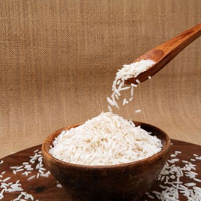 Basmati Standard rice grains pouring from a wooden spoon into a bowl, showcasing their slender shape and white appearance.