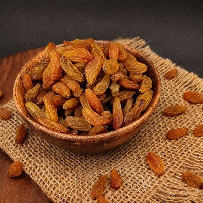 Organic Kishmish raisins in a wooden bowl, showcasing golden-brown dried grapes, wrinkled texture and naturally sweet flavor.