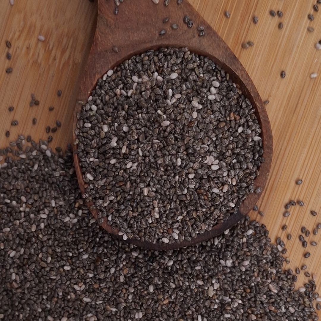 Black chia seeds arranged in a rustic wooden spoon, highlighting their distinctive dark colour, tiny size and natural texture