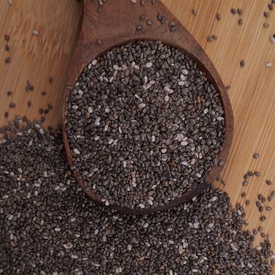 Black chia seeds arranged in a rustic wooden spoon, highlighting their distinctive dark colour, tiny size and natural texture