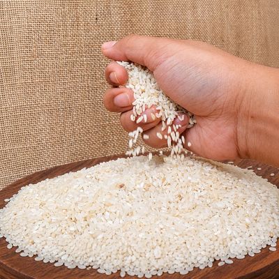Rice Kala Namak grains displayed in hand over a bed of rice, showcasing their distinct short-grain shape, colour and texture.