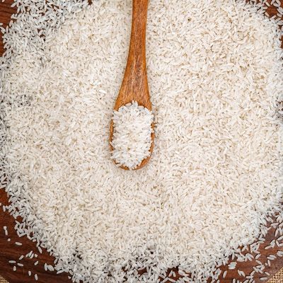Organic Sona Masuri rice grains with a wooden spoon, showcasing fine texture and natural whiteness for everyday Indian meals.