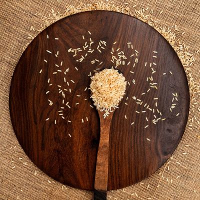 Rice Ratna grains in a wooden spoon on a rustic platter, showcasing their fine, elongated grains and warm natural colour.