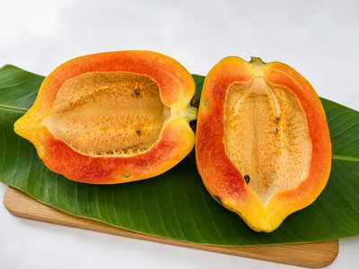 Fresh papaya halves showcasing vibrant orange flesh and seed cavity, arranged on a banana leaf over a wooden board.
