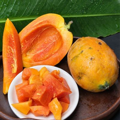 Fresh papaya halves showcasing vibrant orange flesh and seed cavity, arranged on a banana leaf over a wooden board.