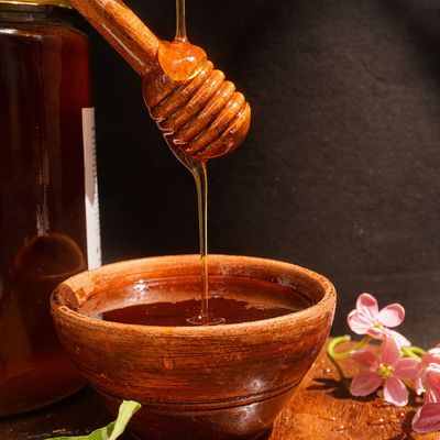 Organic wild small bee honey flows from a wooden dipper into a rustic bowl, showing its rich amber colour, sheen and texture.