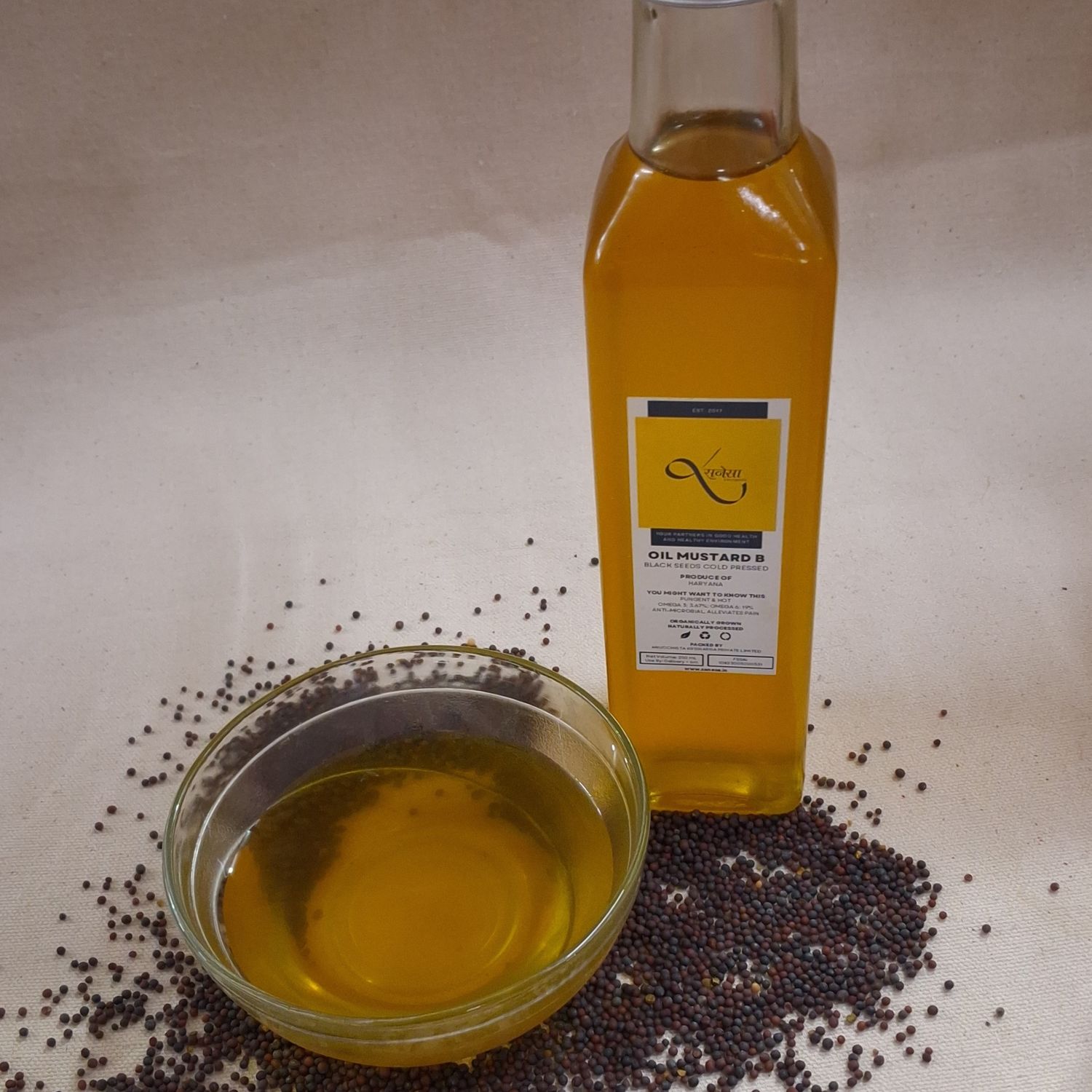 Organic black mustard oil in a glass bottle and bowl, with mustard seeds displayed, showcasing its rich golden color.