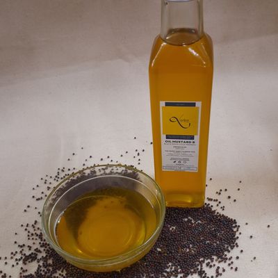 Organic black mustard oil in a glass bottle and bowl, with mustard seeds displayed, showcasing its rich golden color.