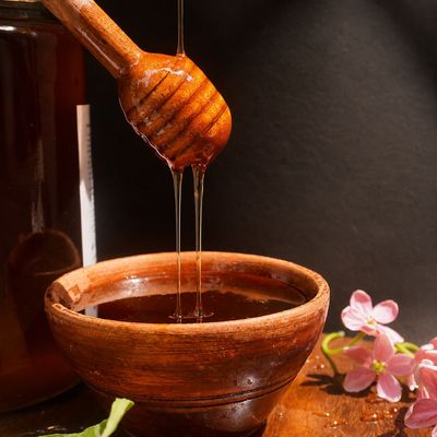 Organic Sundarbans wild honey flowing from a wooden dipper into a bowl, highlighting its rich amber colour and texture, pure!