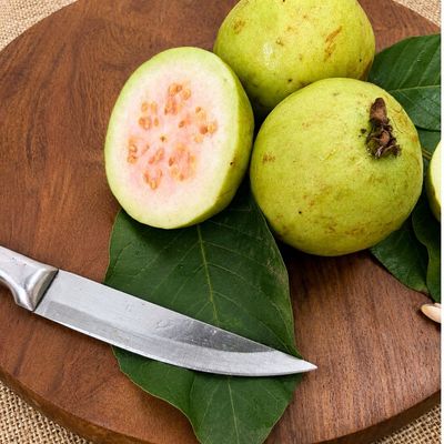 Organic pink guava, whole and cut open to show its soft, pink flesh and seeds, arranged with fresh leaves on a wooden board!
