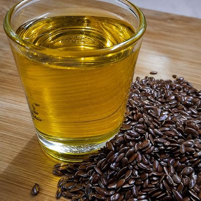 Organic flaxseed oil in a glass, golden and clear, with glossy brown flax seeds beside it, showcasing its rich natural color.