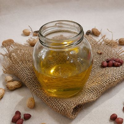Organic peanut oil in a clear glass jar, golden and pure, surrounded by raw peanuts and jute fabric, ideal for daily cooking.