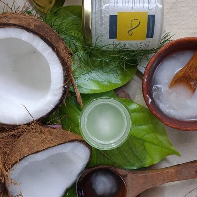 Organic virgin cold-pressed coconut oil with fresh coconut halves, leaves and natural ingredients, ideal for healthy cooking.