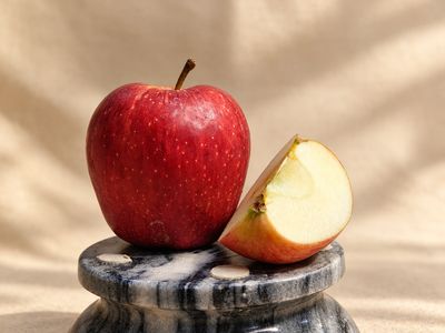 Kinnaur Royal Delicious apple with deep red skin and a fresh-cut wedge revealing creamy white flesh on a black marble stand.
