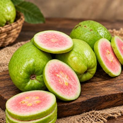 Whole and sliced Japanese Red Diamond Guavas display their naturally pink centres and fresh, firm flesh on a wooden board.