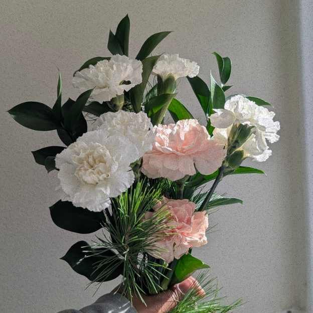 A soft winter bouquet of white and blush carnations with pine and lush greenery, held in natural light for Coco Fleur.co