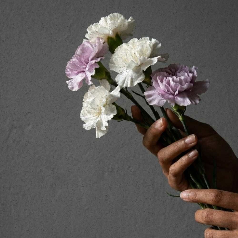 Small hand-tied bundle of white and stone-lilac blooms held against a neutral gray background.