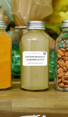 Bottle of Masala Almond Latte with scattered turmeric, and almonds