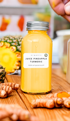 Bottle of Pineapple Turmeric Juice with fresh pineapple slices and turmeric root