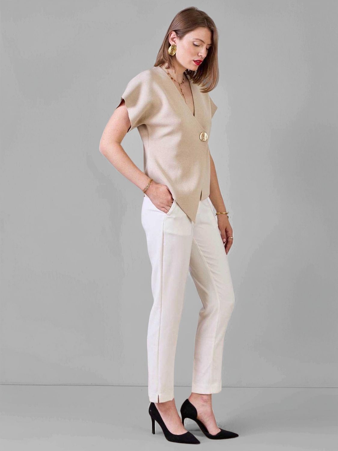 Vue de profil : top beige col V oversize, pantalon blanc droit et escarpins noirs. Look chic minimaliste femme tendance 2025.