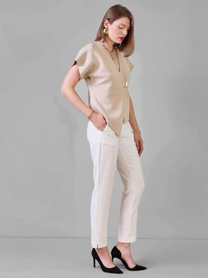 Vue de profil : top beige col V oversize, pantalon blanc droit et escarpins noirs. Look chic minimaliste femme tendance 2025.