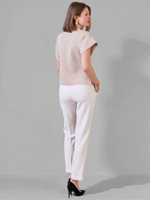 De dos : top beige, pantalon blanc, escarpins noirs. Look chic minimaliste femme 2025.