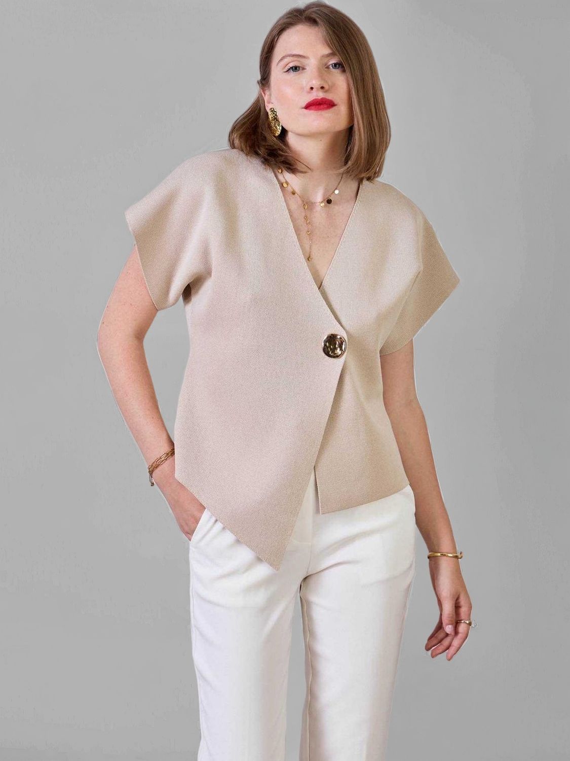 Vue de face : top beige col V oversize avec bouton doré, pantalon blanc droit. Look femme chic minimaliste tendance 2025.