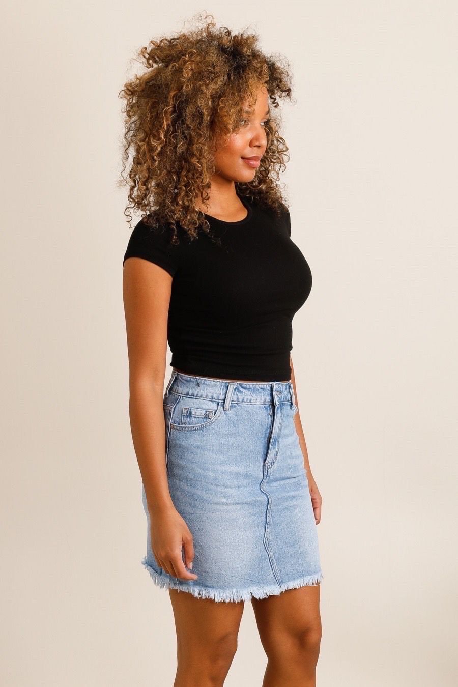 Vue de profil : mini-jupe en jean bleu clair taille haute, finition effilée. Look casual femme tendance été 2025.
