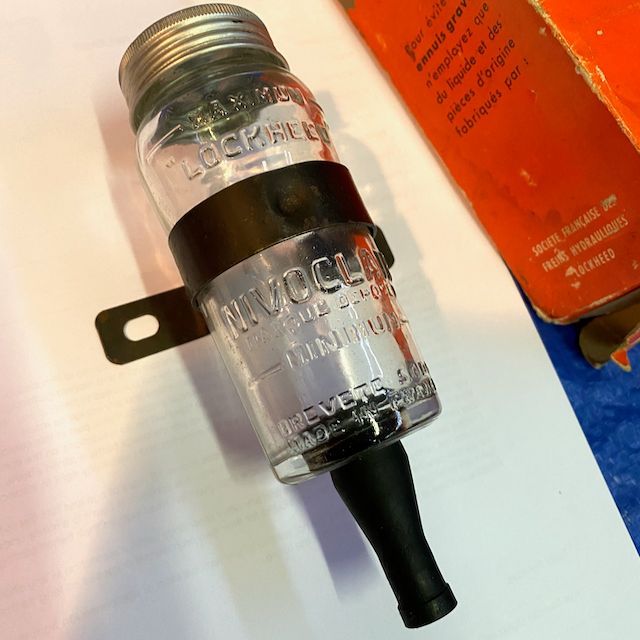 A Peugeot 203 brake fluid reservoir with attaching clamp. This essential part stores your vehicle&#39;s brake fluid and protects it from dirt and moisture contamination.