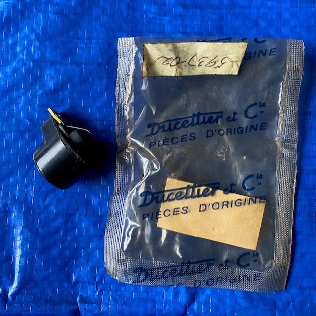 &quot;A Peugeot 203 Ducellier distributor rotor enclosed in a clear plastic bag, placed against a solid blue background. It is responsible for transferring voltage from the ignition coils to the engine&#39;s cylinders, thus igniting the fuel-air mixture within the cylinders.