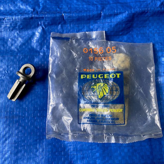 A Peugeot engine coolant drain cock enclosed in a clear plastic bag, placed against a solid blue background. The drain cock is a small, black plastic component designed for automotive use, with visible threads and a turning mechanism