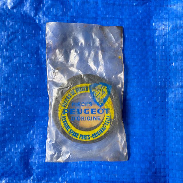 A Peugeot 203 403 front hub seal enclosed in a clear plastic bag, placed against a solid blue background. The front hub seal keeps the wheel bearing lubricant within the wheel end.