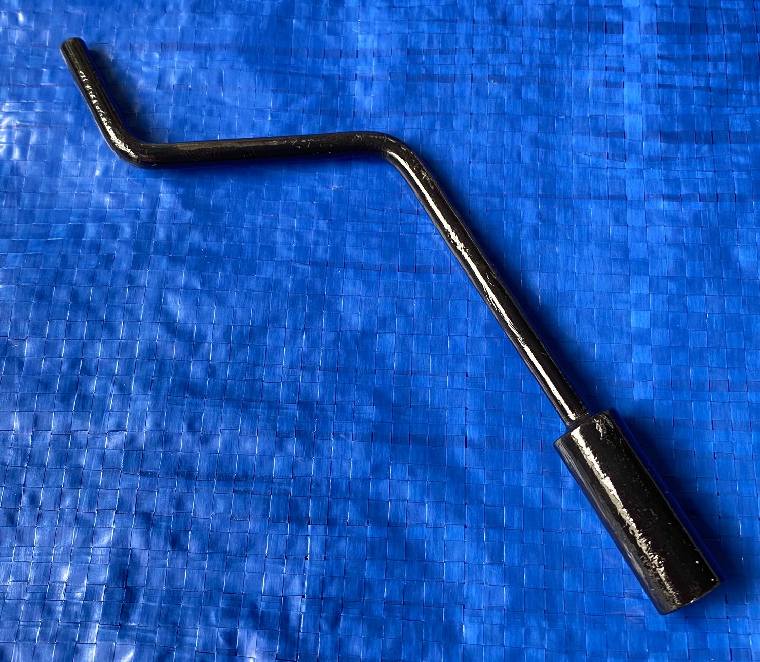 A Peugeot 203 emergency windscreen crank handle placed against a solid blue background. The windscreen crank handle is to open and close a car window: 