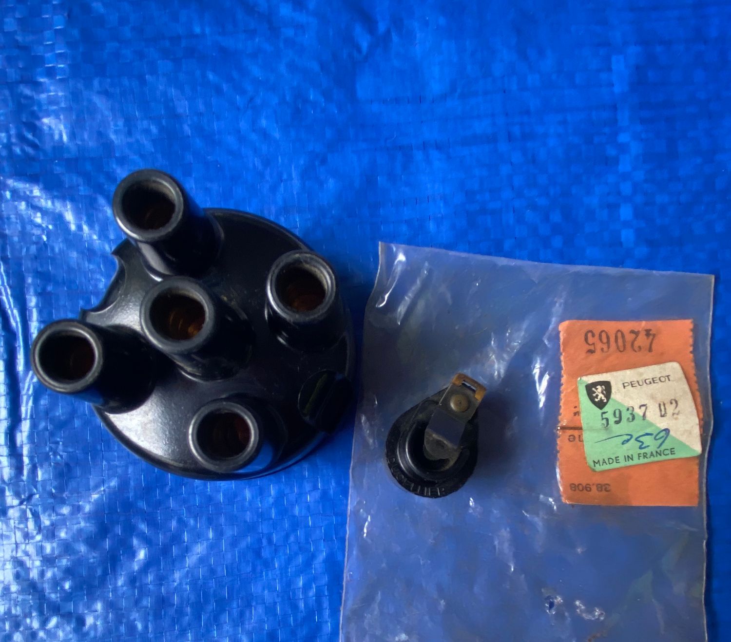 A Peugeot 203 403 distributor cap and rotor placed against a solid blue background. The distributor cap and rotor are responsible for transferring voltage from the ignition coils to the engine&#39;s cylinders, thus igniting the fuel-air mixture within the cylinders