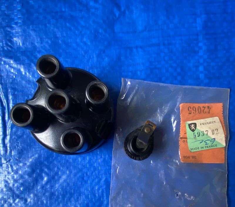 A Peugeot 203 403 distributor cap and rotor placed against a solid blue background. The distributor cap and rotor are responsible for transferring voltage from the ignition coils to the engine&#39;s cylinders, thus igniting the fuel-air mixture within the cylinders