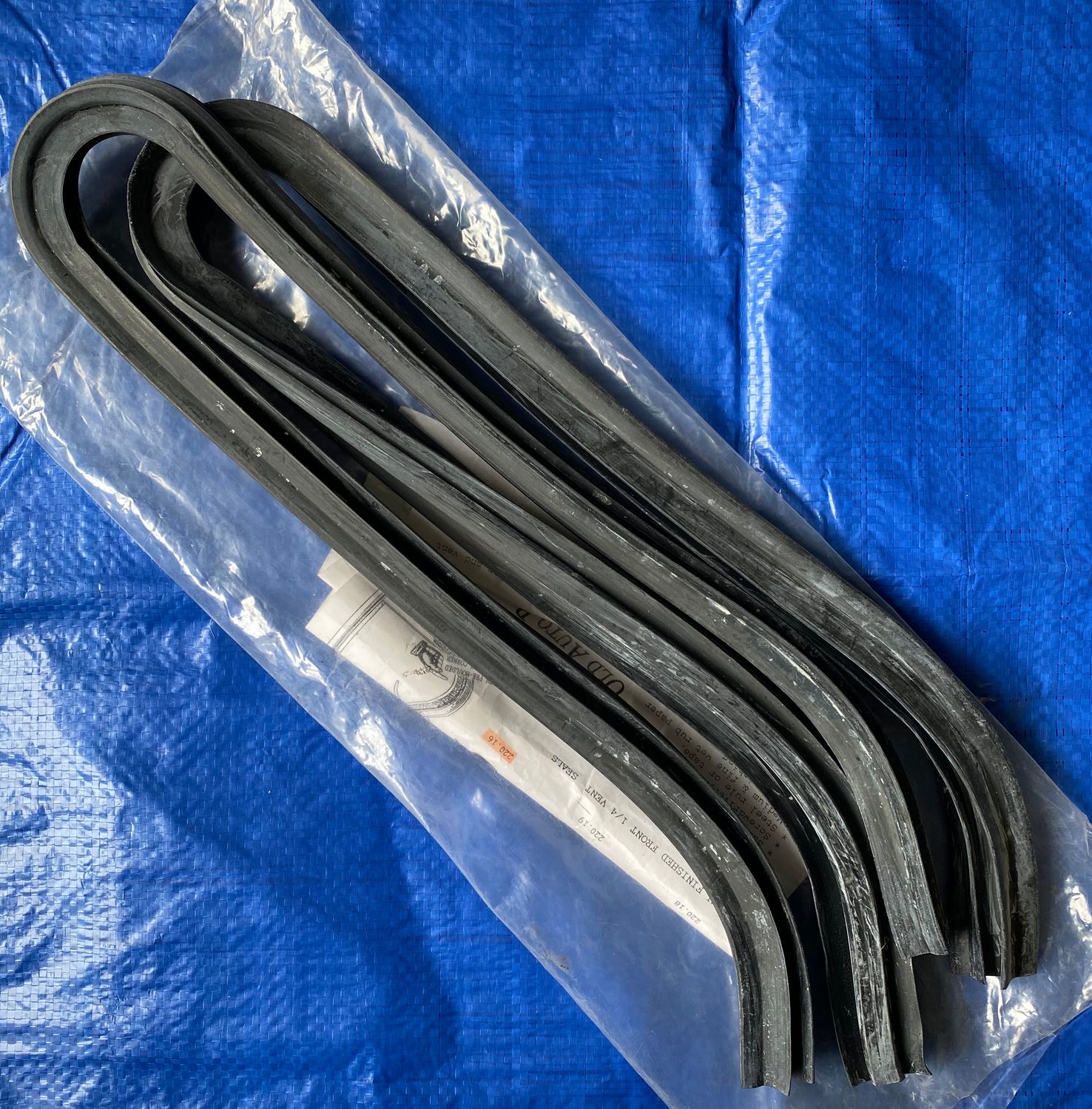A pair of Peugeot 203 front quarter window seals enclosed in a clear plastic bag, placed against a solid blue background. Front quarter window seals, also known as weather stripping insulate, protect, and keep the window glass in place. 
