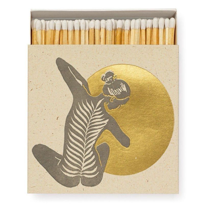 Matchbox design by Archivist Gallery offered by Maison Maeva featuring a minimalist yogi seen on the back gracefully stretching toward a full shiny golden moon. This design highlights the human form as part of nature. Contains 100 matches, each 100mm long, in a box measuring 110 x 110 x 50mm.