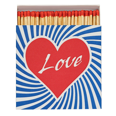 Love Matches by Archivist Gallery, offered by Maison Maeva, featuring a red heart and blue-white stripes around it in bright colors, inspired by 1970s style. Contains 100 matches (100 mm) in a 110 x 110 x 50 mm box.