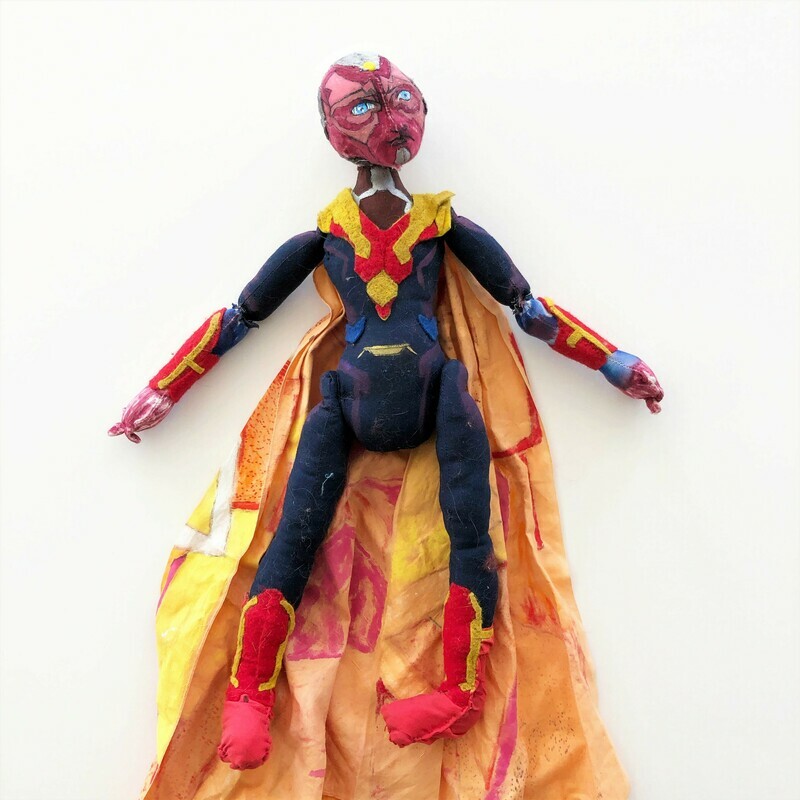 SUBMISSION Vision is a 20&quot; doll of the superhero Vision. Vision has a red face and neck with a green section over a half his head and ears. In the center of his forehead is a yellow gem embroidered onto him. He also has striking blue eyes. Vision&#39;s body is green with his forearms and lower legs red with gold lines across them. His cape is yellow with hints of red and drapes over his shoulders and are held together by a red x across his chest. 