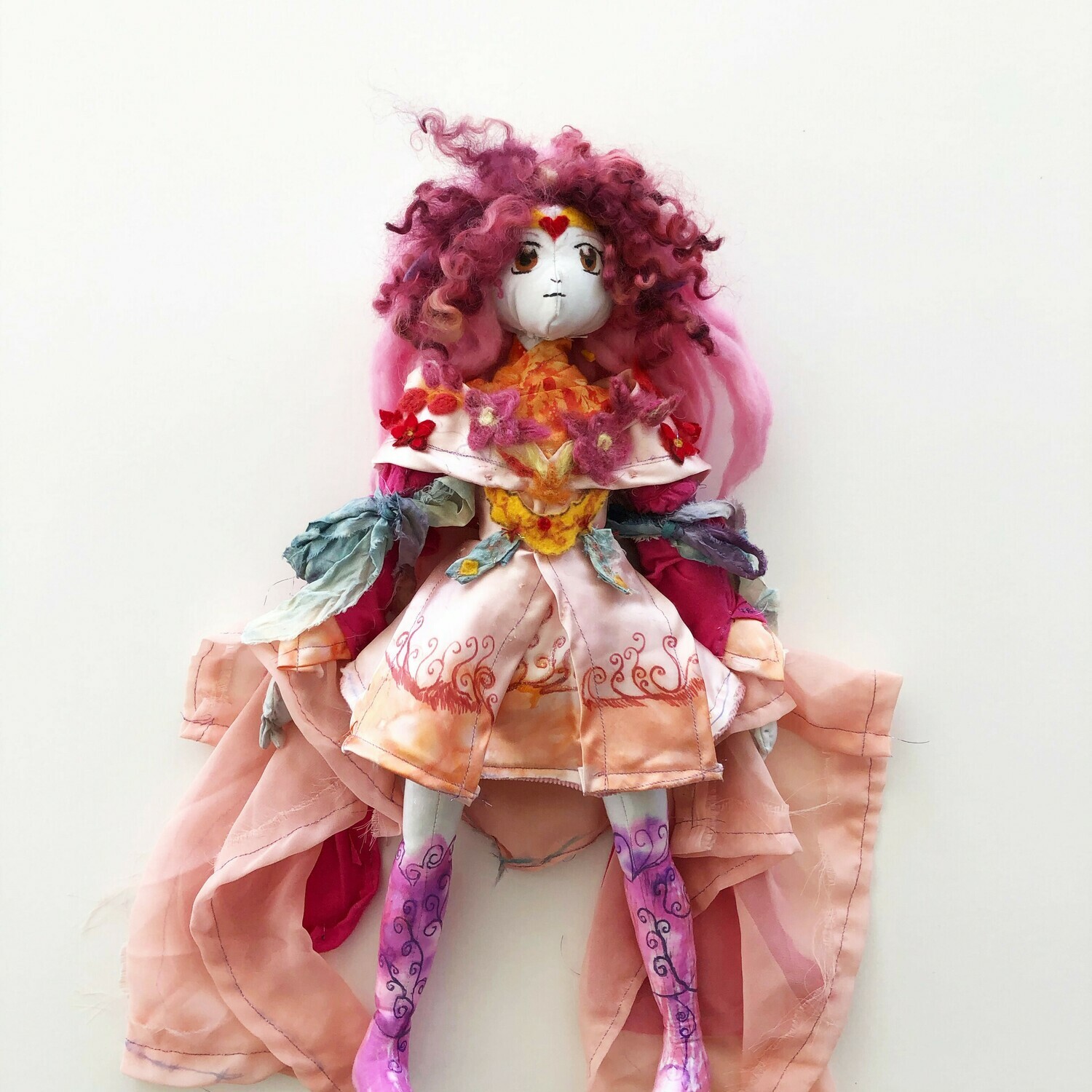 SUBMISSION Wanda is a 20&quot; tall magical girl doll version of the superhero Scarlet Witch. The doll sports mid-length pink curly hair. She has large eyes, small lips/ nose, and a golden headband with a heart in the center. She wears a long pink cloak with flowing fabric down the sleeves.  On the collar are pink and red hand embroidered flowers. On her sleeves are blue bows over red fabric that descend down to her wrists. She has light blue gloves on. Her dress is a light pink with a golden crest in the center. the Bottom is an orange-pink with a red swirl rising up the skirt of the dress. She has bright pink knee high boots on. These boots have blue swirl vines wrapped around them.  