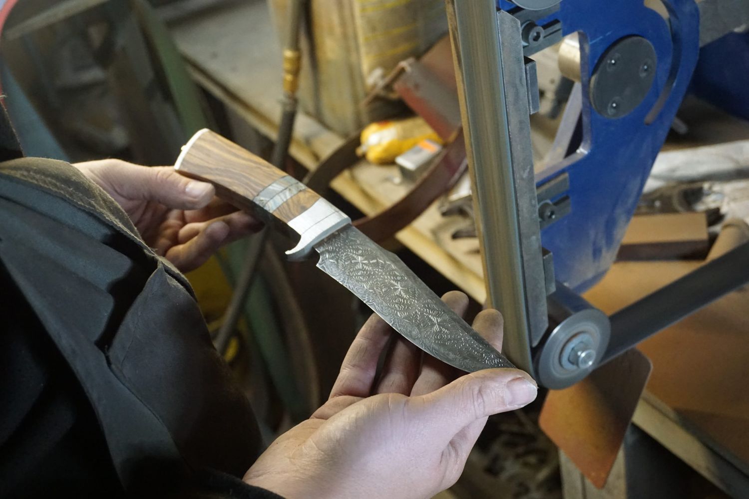 Knifemaker shaping a fossil and wood knife handle on a belt grinder