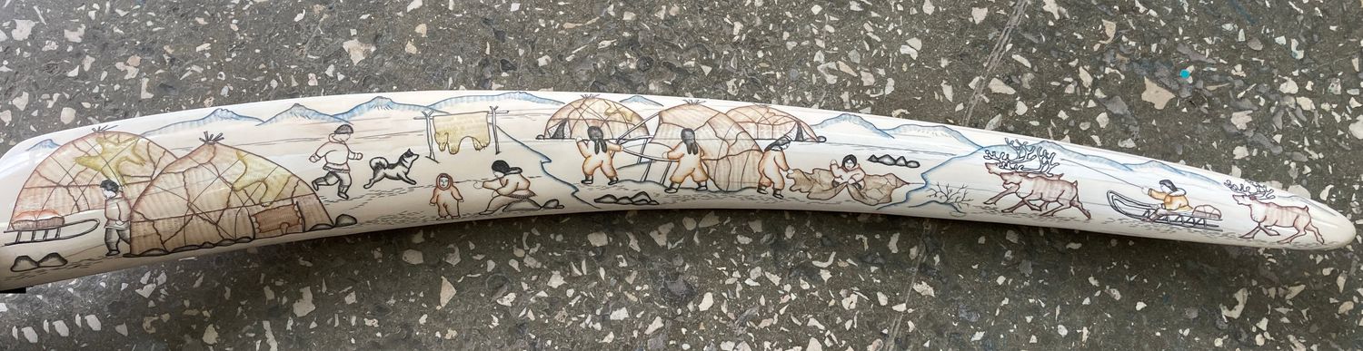 Traditional scrimshaw engraving by a Uelen master on walrus ivory, depicting scenes of Eskimo daily life, hunting activities, sled dogs, and Arctic coastal traditions.