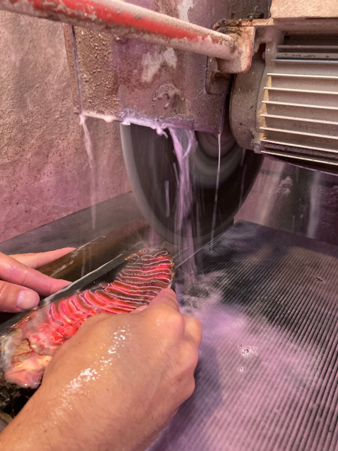 Cutting a stabilized mammoth tooth block on a water-cooled stone-cutting saw for custom knife handle scales.