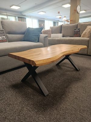 Coffee table with wavy side lines, faux wood top, and black legs. Dimensions: 110 x 60 x 43 cm.  Manx Mēbeles
