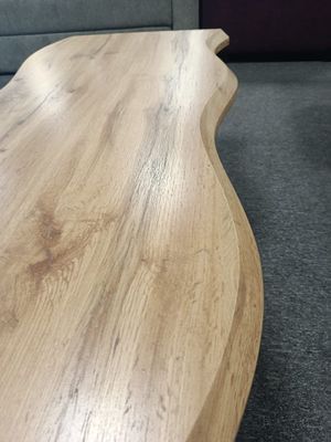 Coffee table with wavy side lines, faux wood top, and black legs. Dimensions: 110 x 60 x 43 cm.  Manx Mēbeles