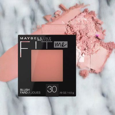 A black compact of Maybelline New York Fit Me Blush in Rose displayed alongside a lightly crushed pink powder, highlighting its soft, natural hue.