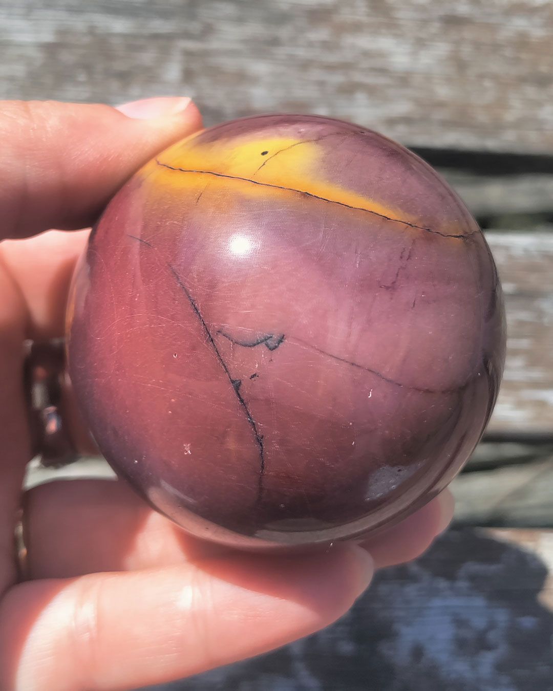 Mookaiet bol van 280 gram met diepe roodtinten en warme oranje aders, gefotografeerd in zonlicht