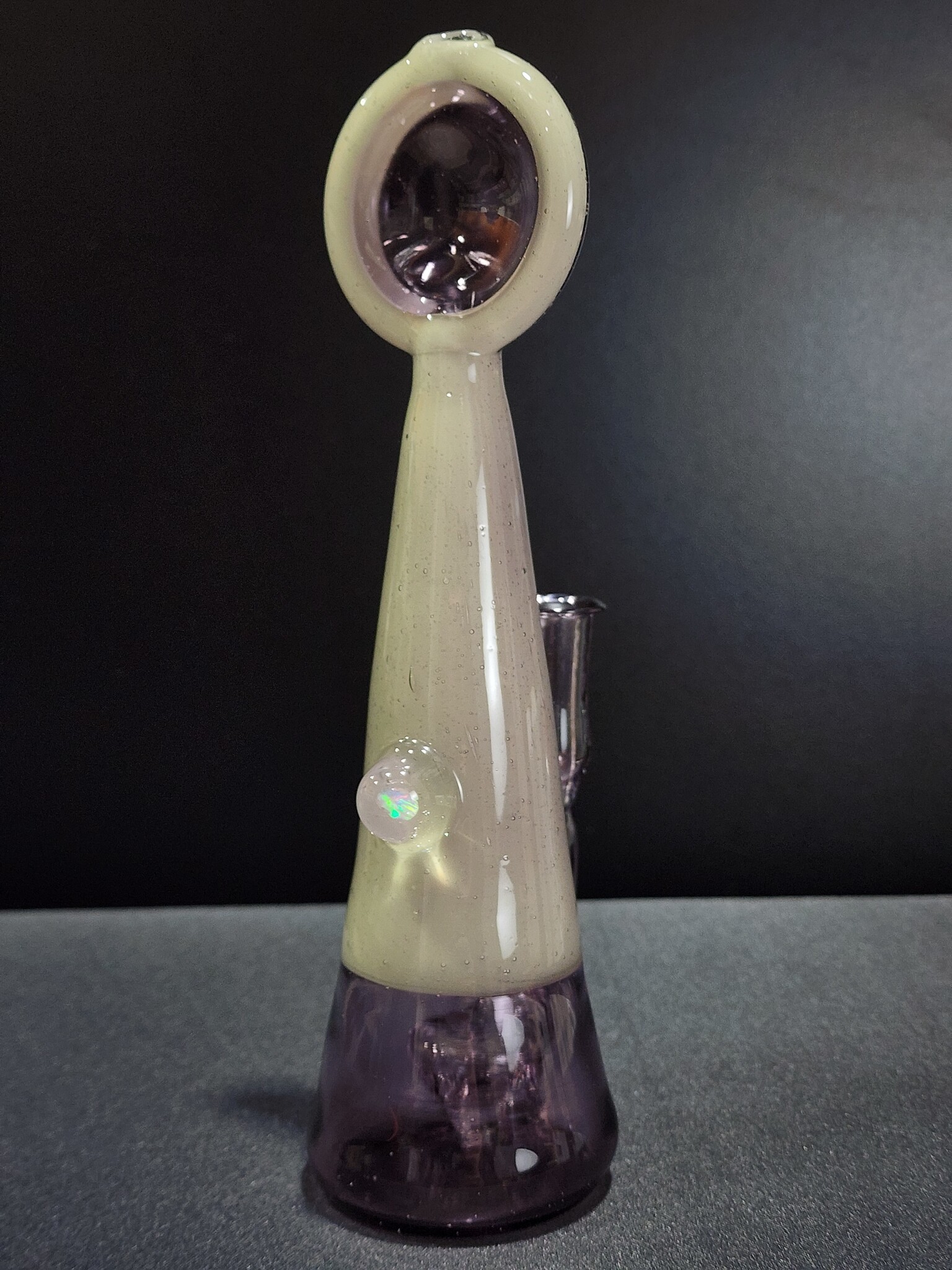 Tall conical glass piece in pale cream and translucent purple glass, with a small iridescent opal set in a clear glass dome on its side