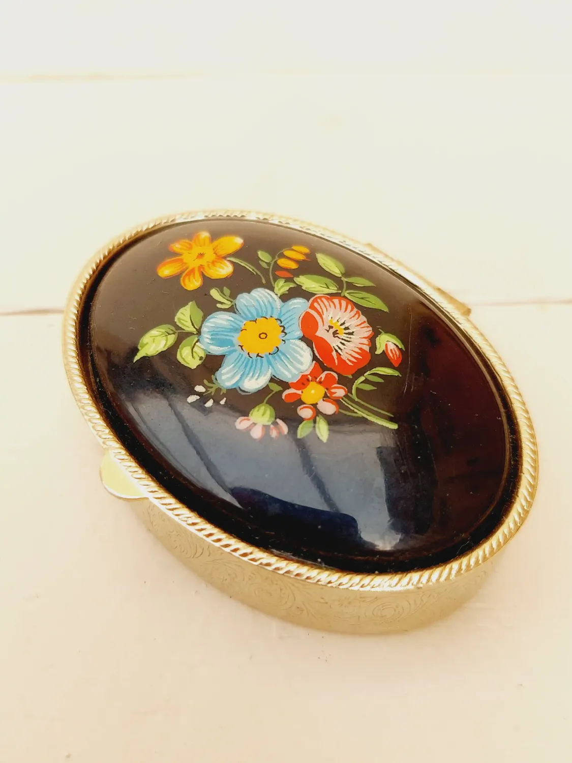 Vintage ovaal pillendoosje, zwart deksel met veldbloemen, goudkleurig doosje
